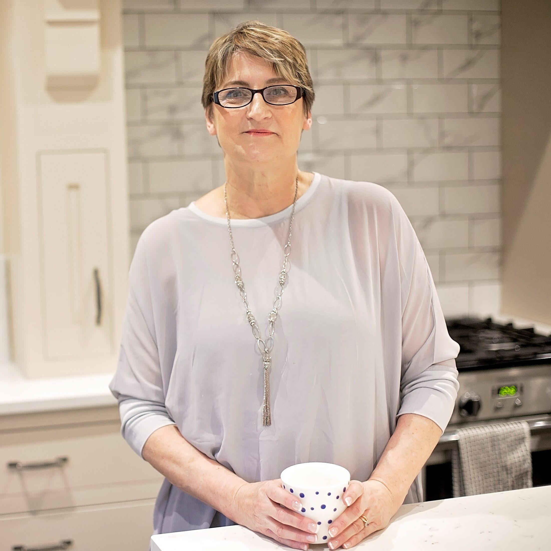 Picture of Denise Fowler holding a cup of tea in a grey top